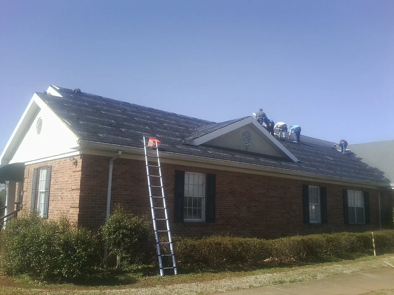 Crew tearing shingles off a brick ranch roof with a ladder set — Emergency Roof Repair work by our crew in Bayonne