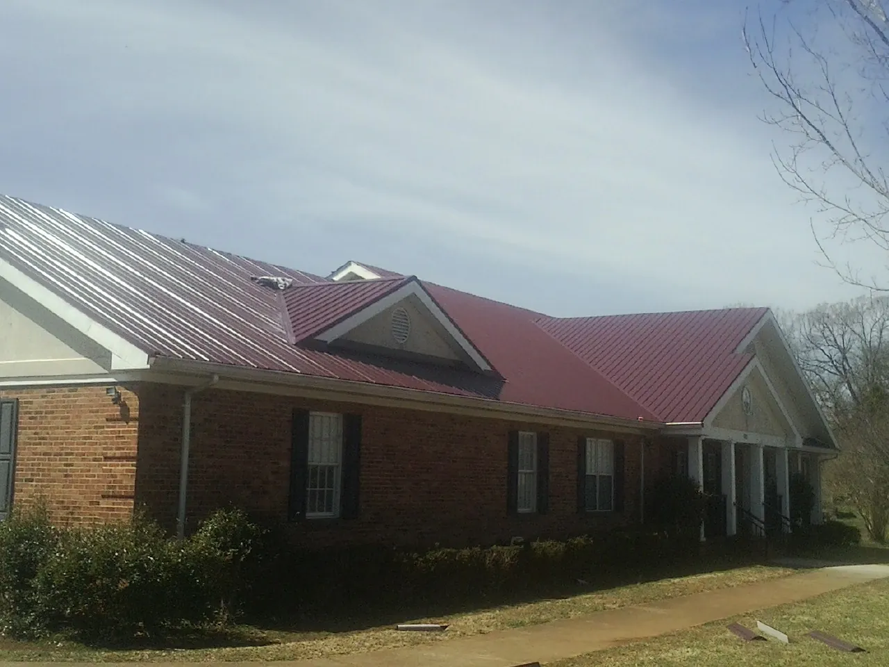 Red metal roof with gabled entries on a long brick building, from a Hail Damage Roof Repair job in Bayonne