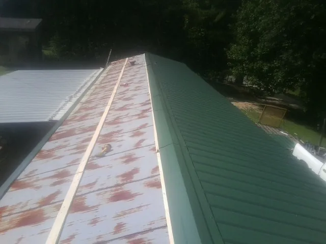 Old rusted panels beside newly installed green metal roofing — Wind Damage Roof Repair by Roofing Brothers in Bayonne