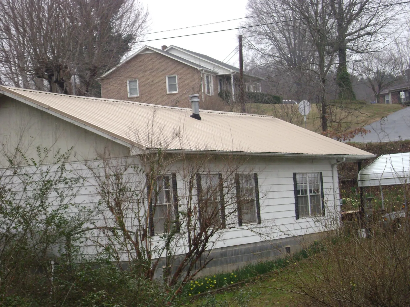 Tan metal roof on a white sided house set into a hillside — Commercial Roofing by Roofing Brothers in Bayonne